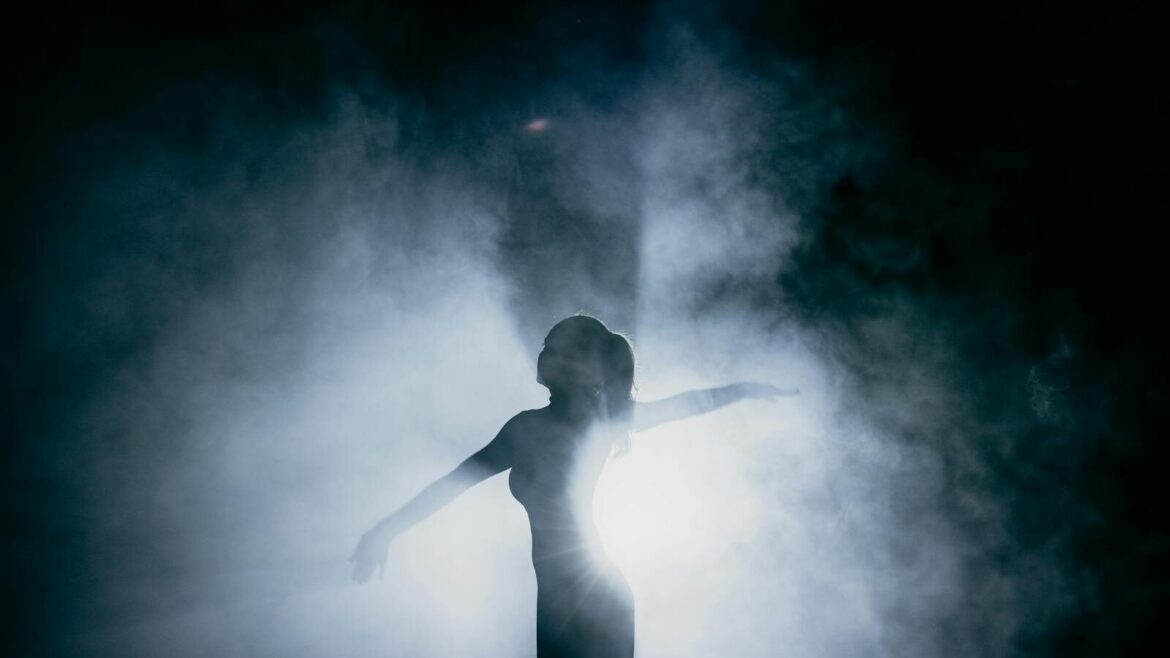 Captivating silhouette of a dancer gracefully posing amidst smoke, illuminated by dramatic backlight.