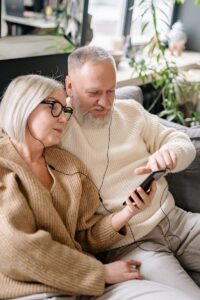 Happy senior couple sharing music on a mobile phone, cozy indoors.