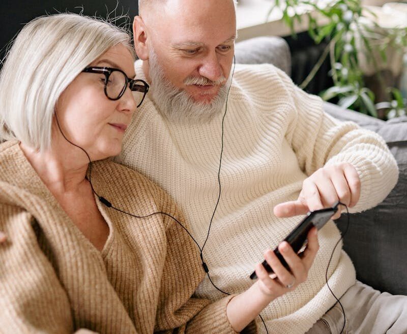 Happy senior couple sharing music on a mobile phone, cozy indoors.